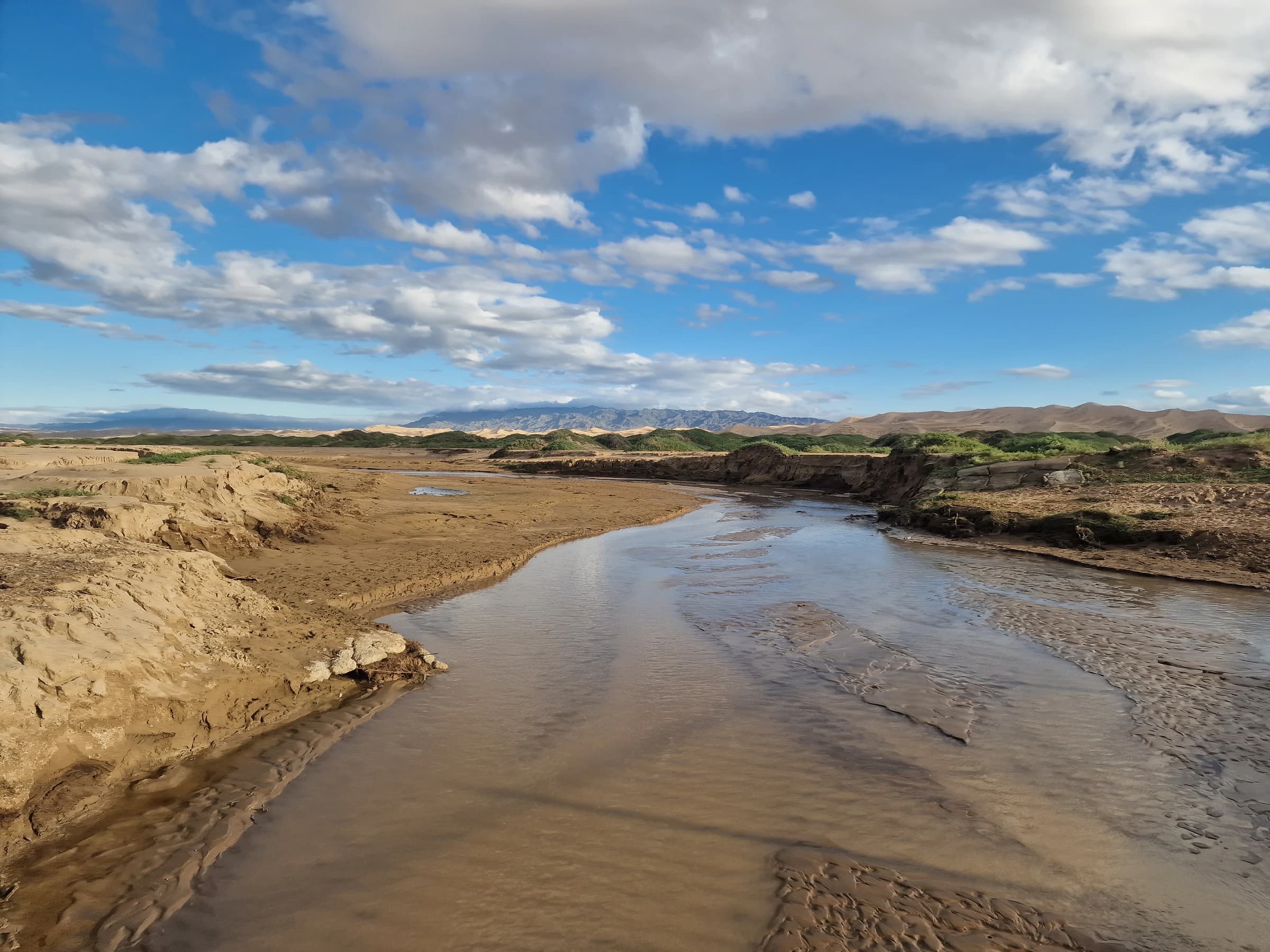 A winding river crossing the Gobi landscape beneath a wide blue sky